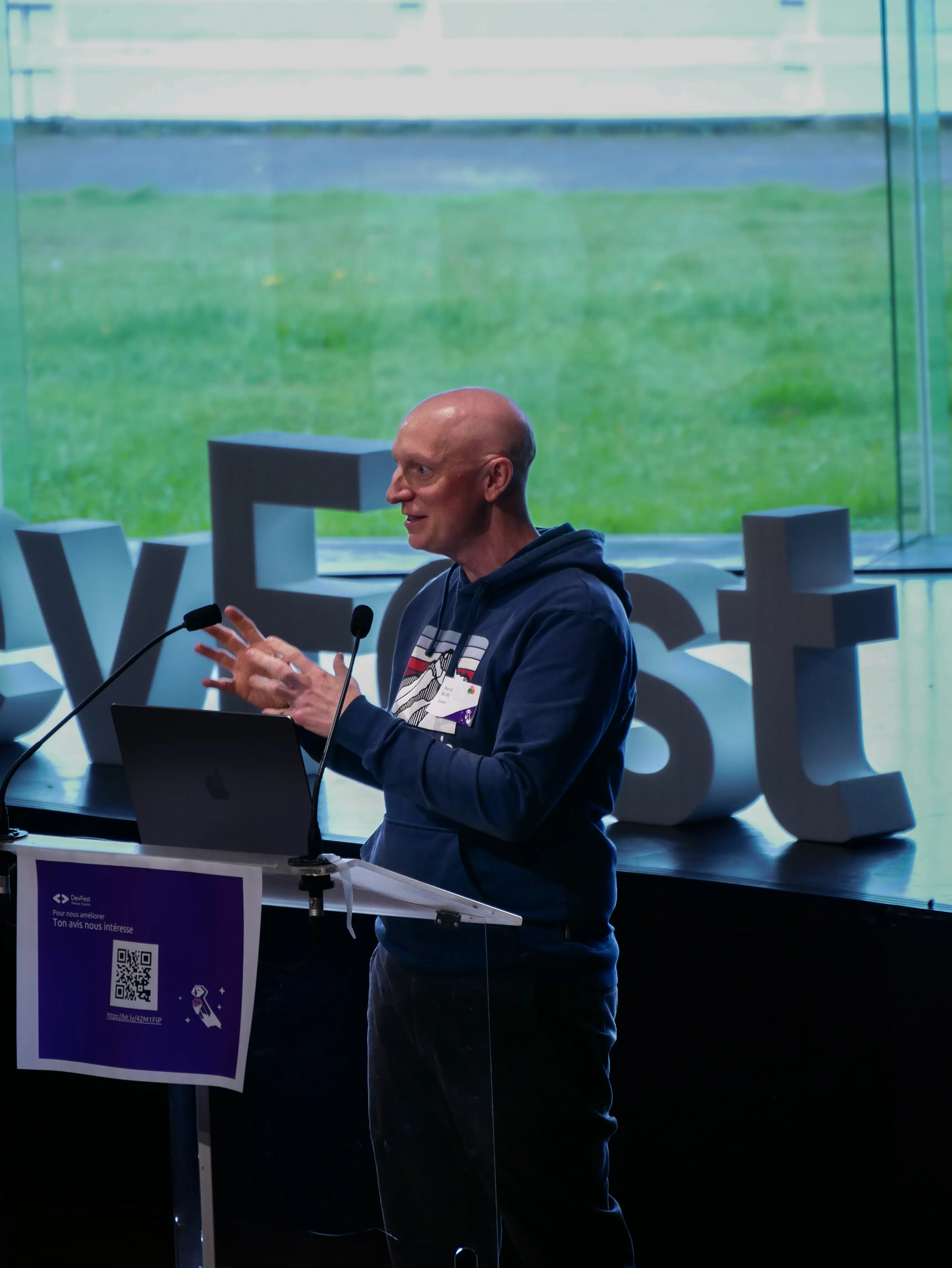 Speaker gesturing at podium with coastal landscape visible through windows